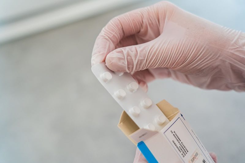 Gloved hand checking a finished medicine carton and blister strip against the approved label