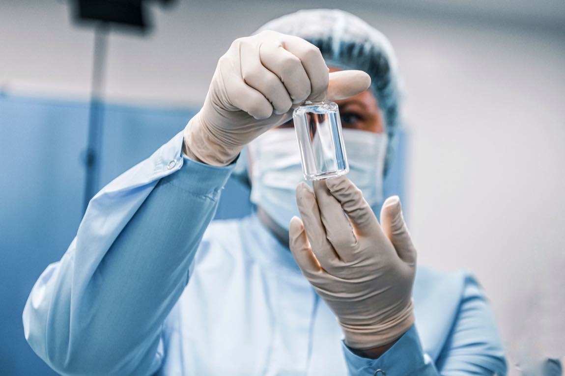 A gowned technician inspecting a vial in a cleanroom