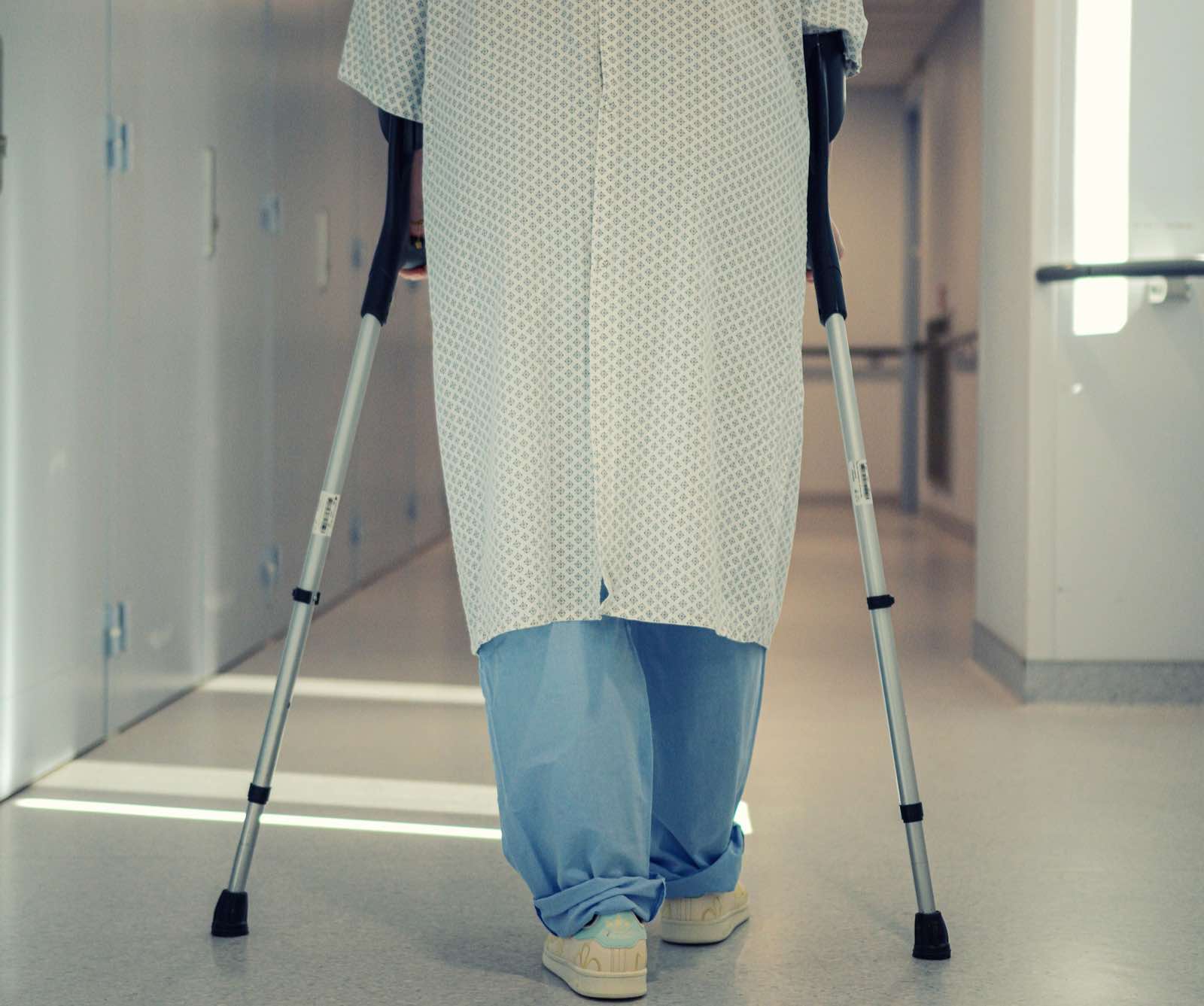 A senior patient using crutches to walk down a hospital corridor, symbolizing recovery and mobility assistance
