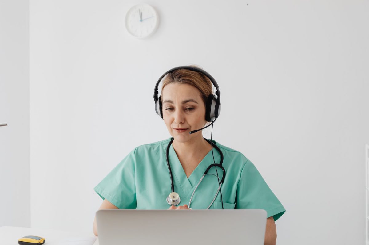 A doctor in scrubs holding a virtual consultation on a laptop