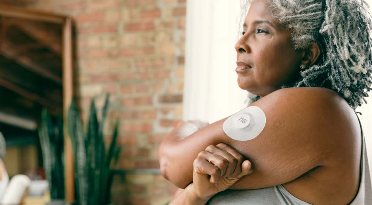 A woman wearing a continuous glucose monitoring sensor on her upper arm