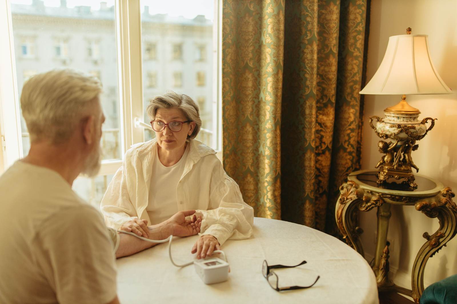A senior woman checking a man's blood pressure at home in warm light