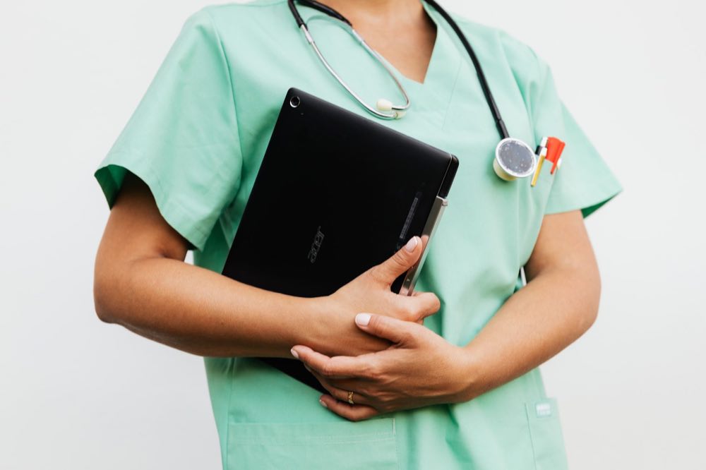 A nurse in green scrubs holding a tablet and stethoscope