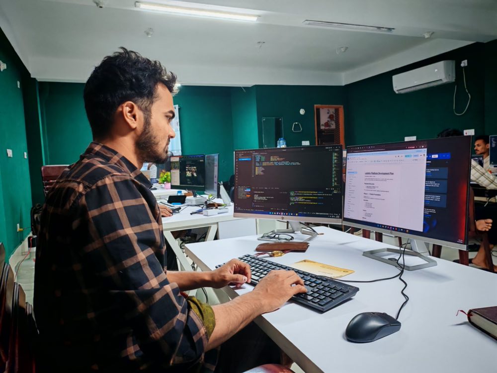 A software developer working at a dual monitor setup in a modern office