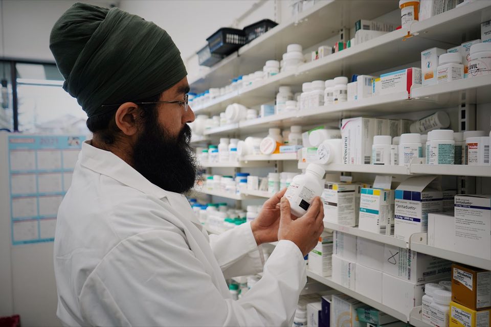 Pharmacist checking stock along shelves of medicines