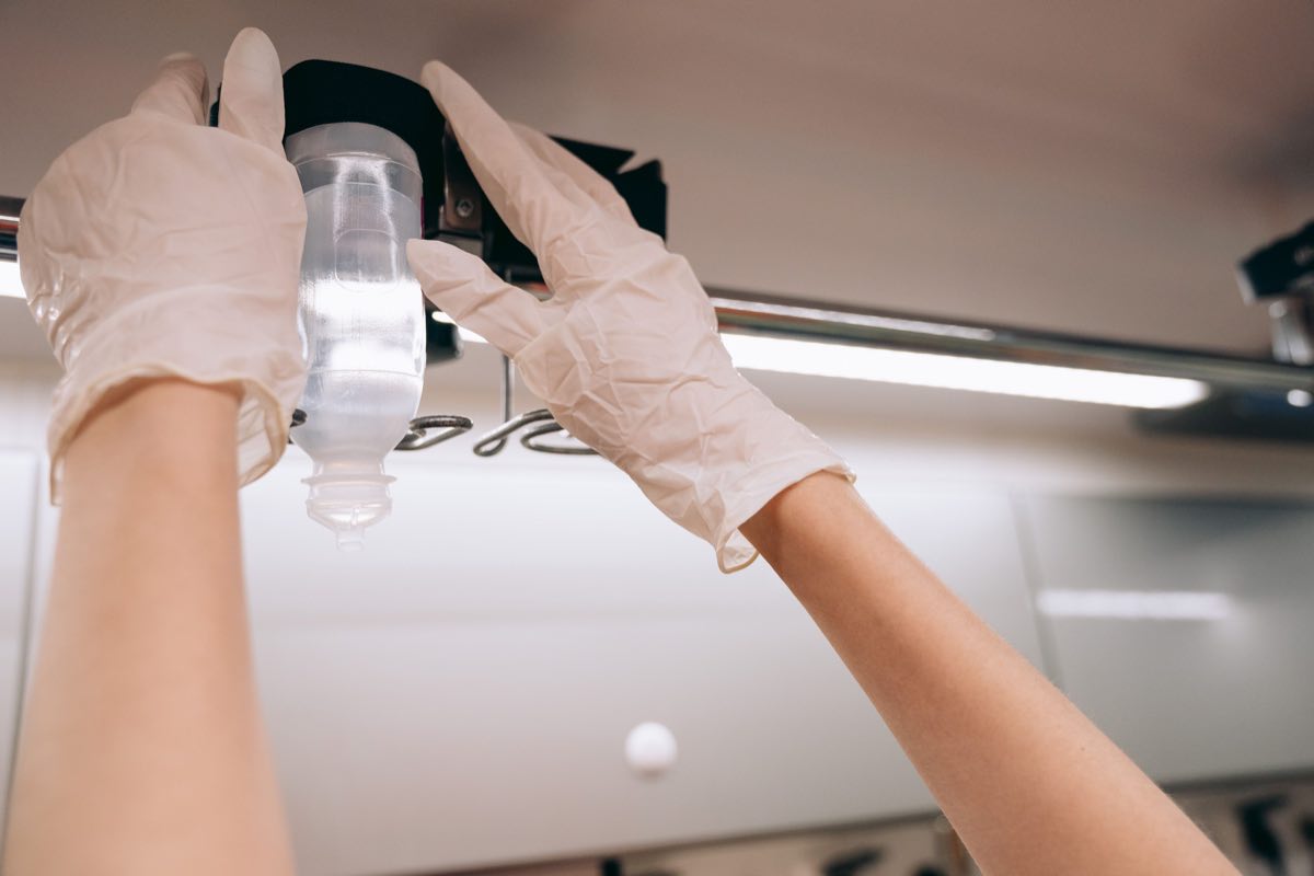Gloved hands adjusting an IV drip in a clinical setting