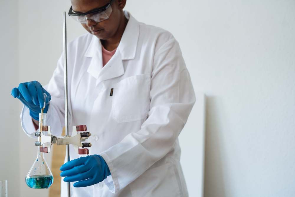 A laboratory technician in uniform and safety glasses at work