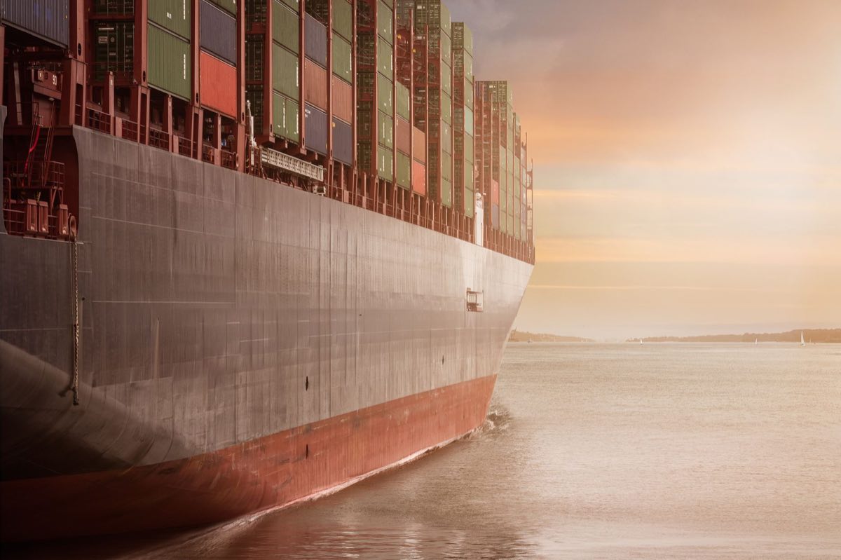 A loaded container ship crossing calm water at dusk
