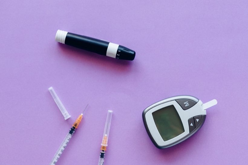 Glucose meter, lancet, and syringes arranged on a lilac surface