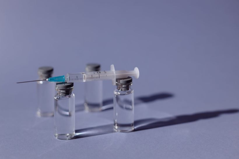 Syringe resting across vaccine vials