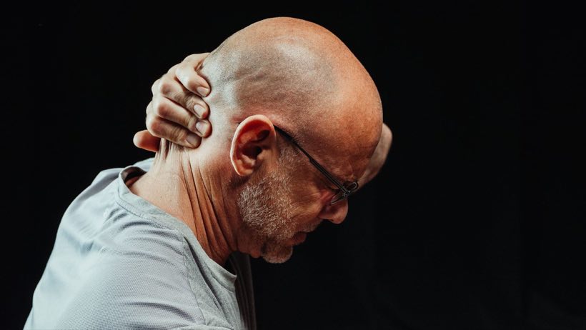 Side view of a man holding his neck in pain against a black background