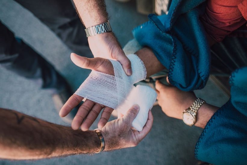 Close-up of two people bandaging an injured hand outdoors, focusing on first aid care