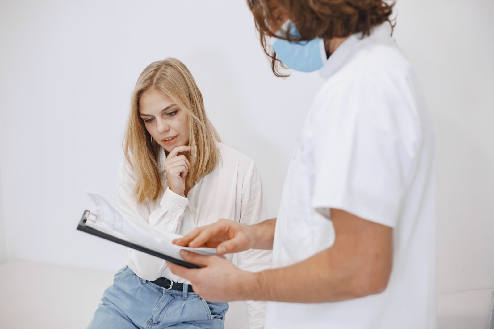 A doctor in a face mask discusses diagnosis with a patient in a clinic setting