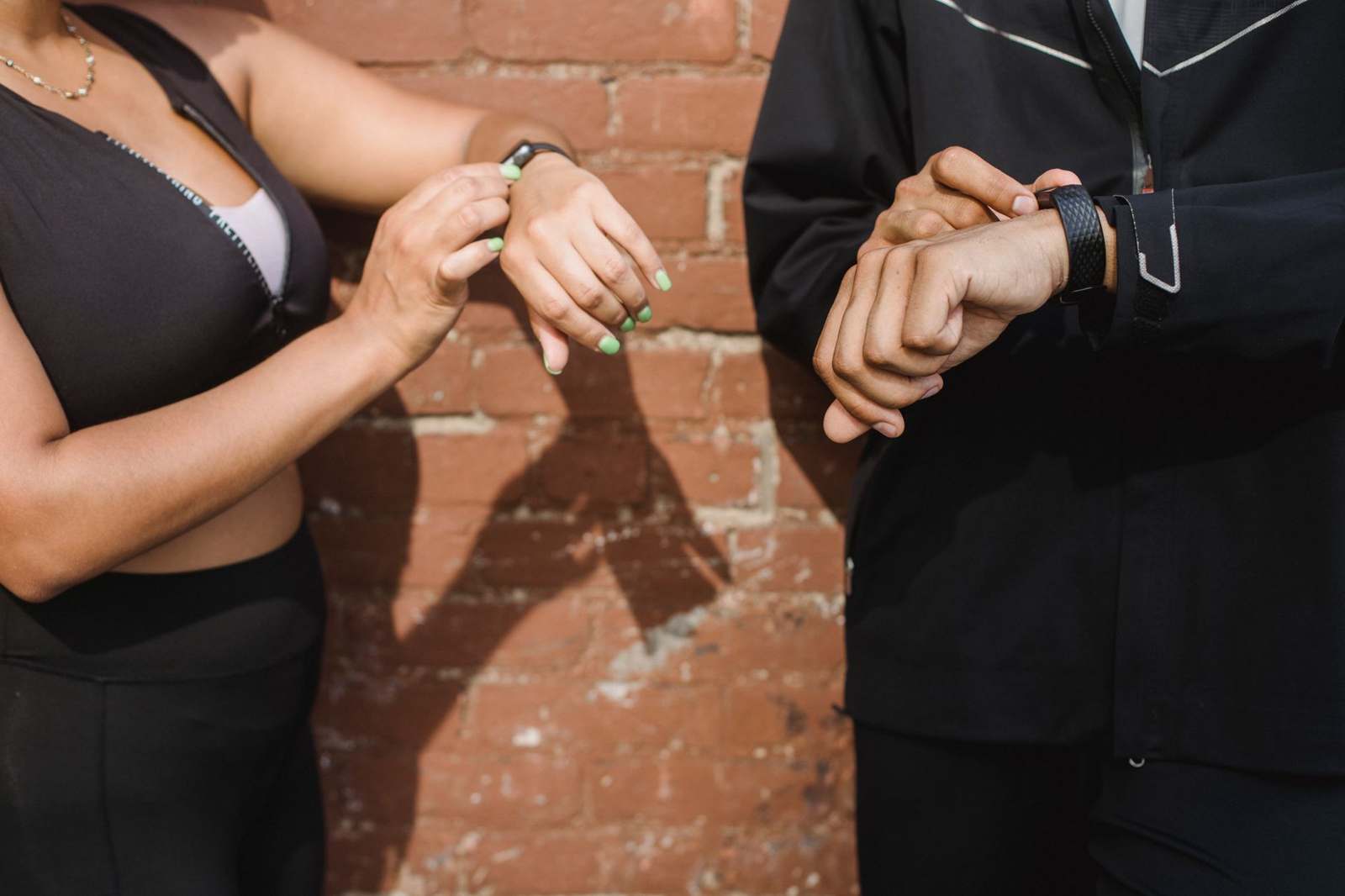 Two people in sportswear checking fitness trackers on their wrists