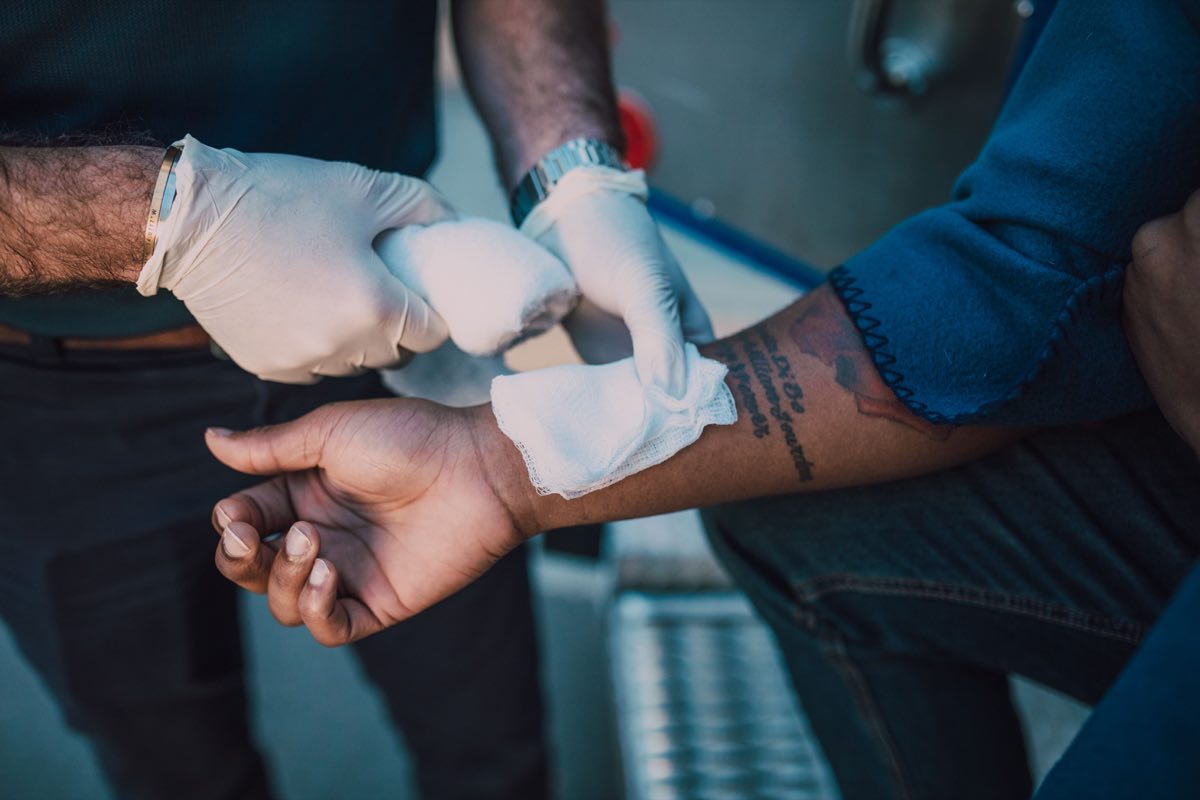 A healthcare professional in gloves applying a bandage to an injured arm, focusing on first aid care